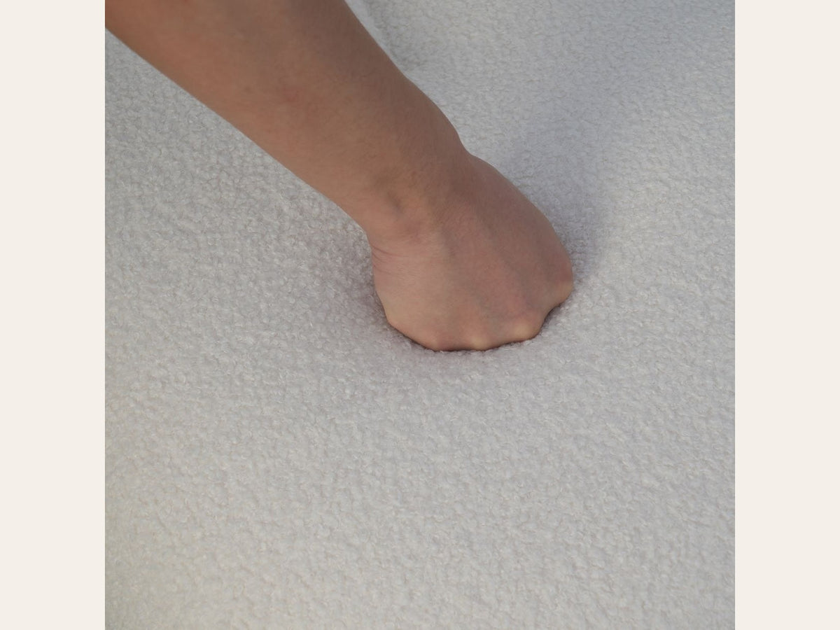 Fauteuil nuage pivotant 360 en tissu bouclette blanc écru, gros plan sur la bouclette, une main s'enfonce dans l'assise