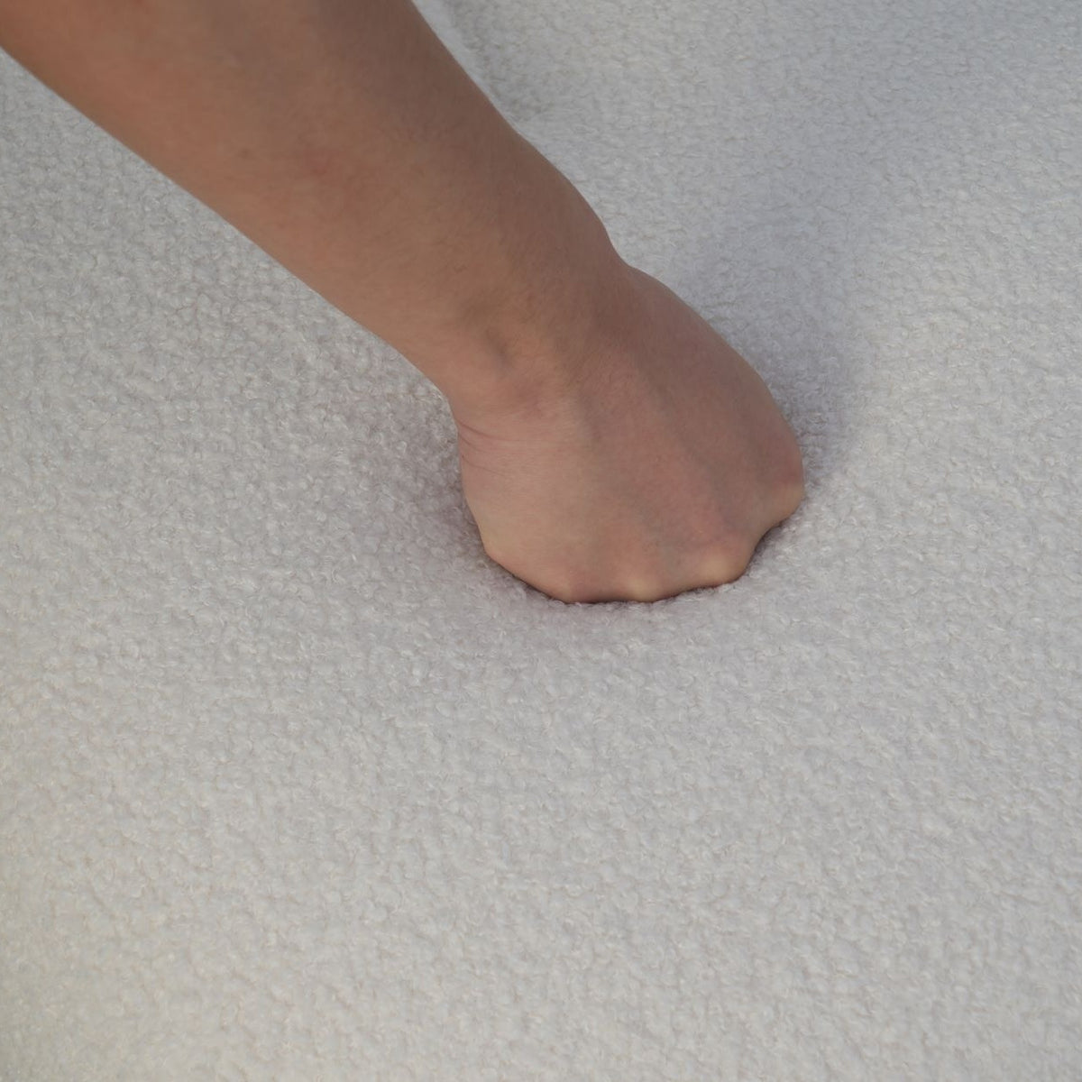 Fauteuil nuage pivotant 360 en tissu bouclette blanc écru, gros plan sur la bouclette, une main s'enfonce dans l'assise