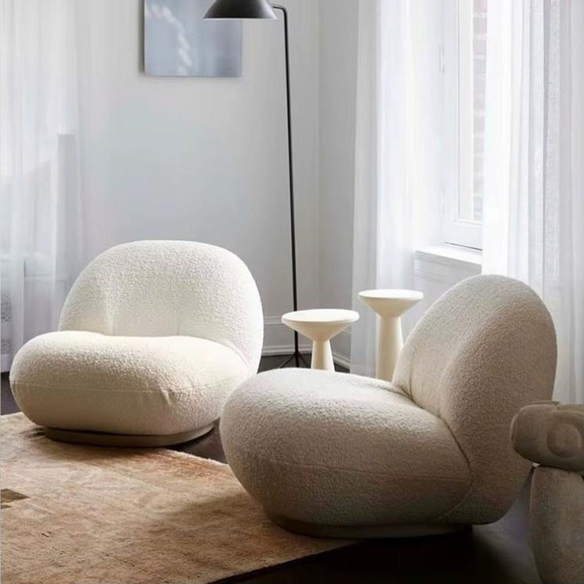 Fauteuil nuage pivotant 360 en tissu bouclette blanc écru, présenté en duo dans un salon, avec lampadaire et tables d'appoint